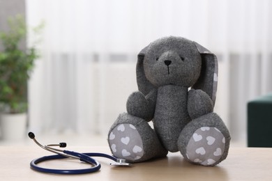 Photo of Pediatrics concept. Toy bunny with stethoscope on table indoors, space for text