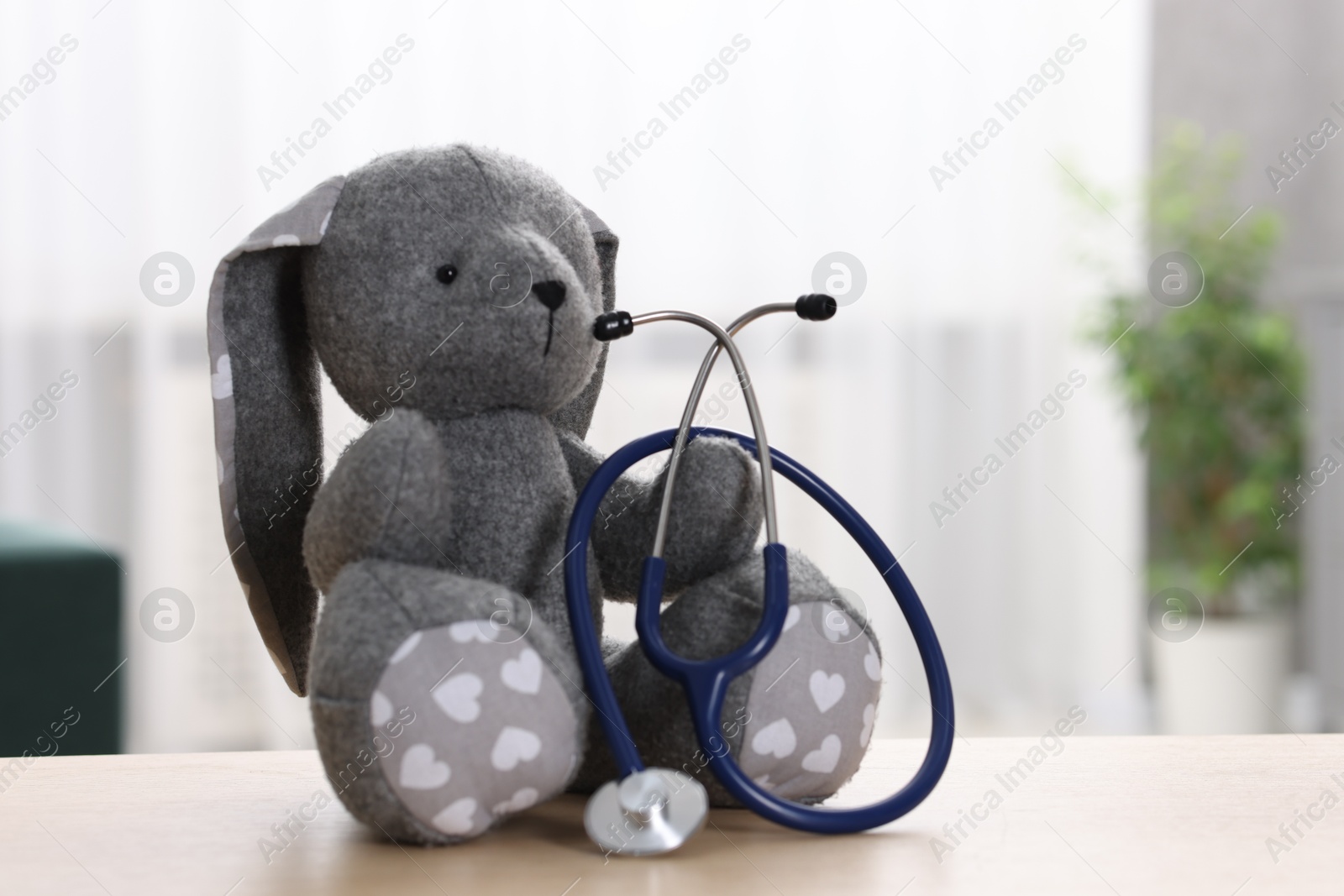 Photo of Pediatrics concept. Toy bunny with stethoscope on table indoors, space for text