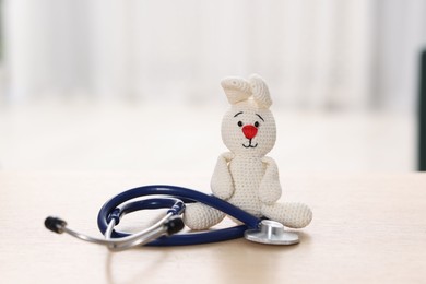 Photo of Pediatrics concept. Toy bunny with stethoscope on table indoors