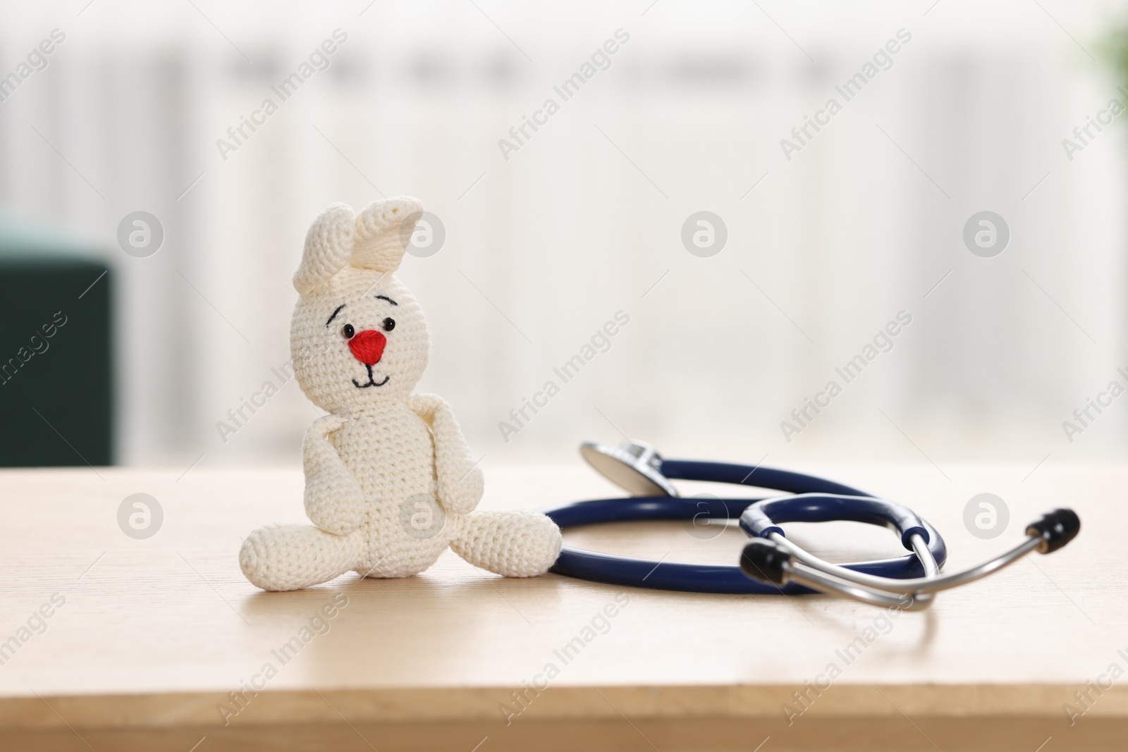 Photo of Pediatrics concept. Toy bunny with stethoscope on table indoors