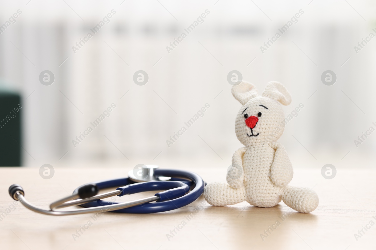 Photo of Pediatrics concept. Toy bunny with stethoscope on table indoors