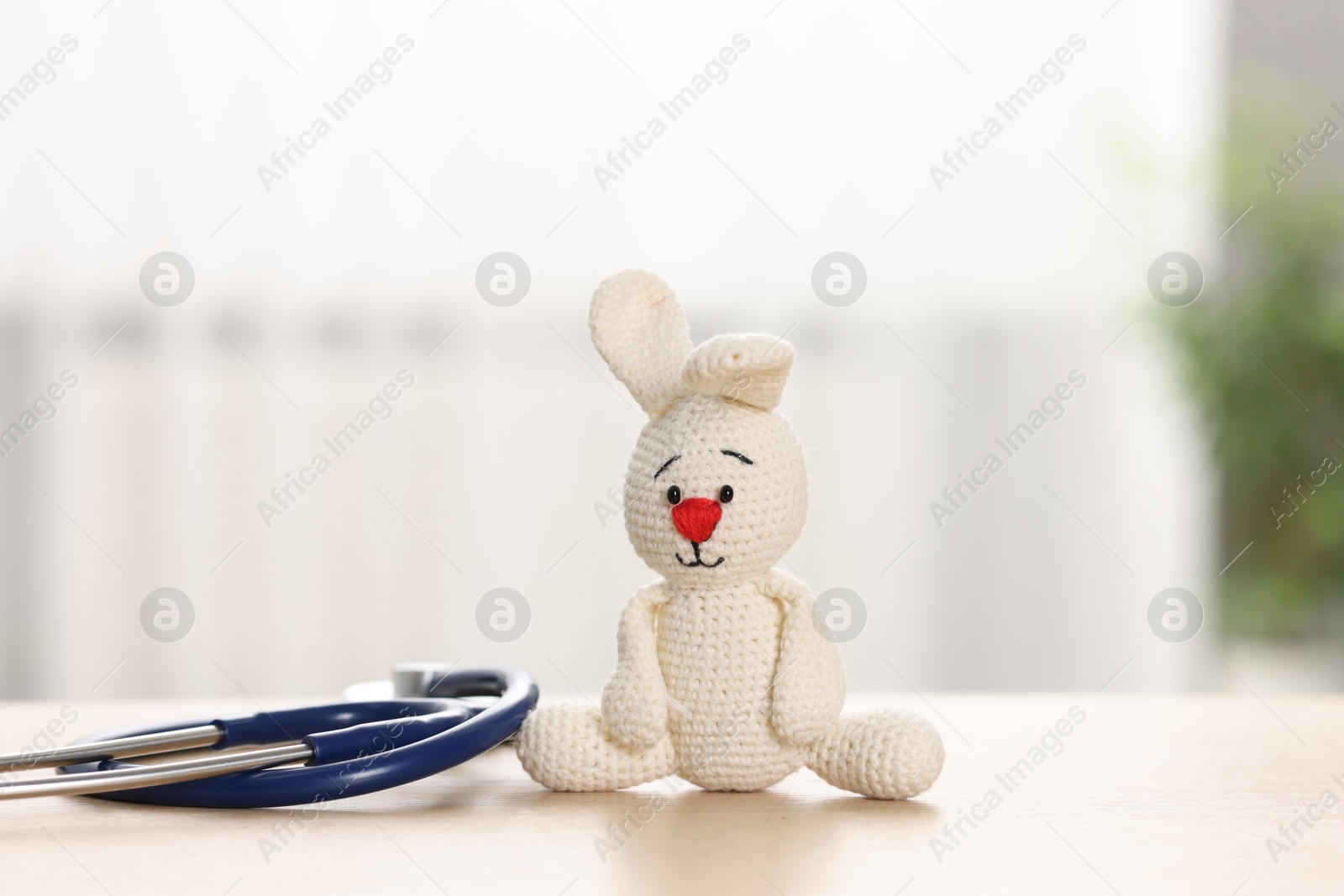 Photo of Pediatrics concept. Toy bunny with stethoscope on table indoors