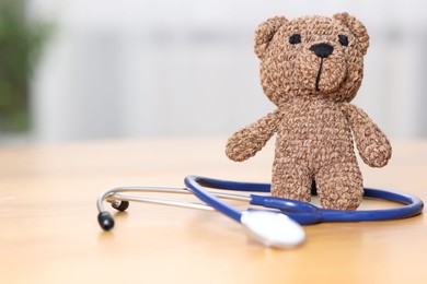 Photo of Pediatrics concept. Toy bear with stethoscope on table indoors, closeup. Space for text