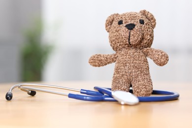 Photo of Pediatrics concept. Toy bear with stethoscope on table indoors, space for text