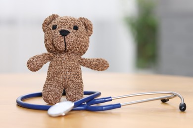 Photo of Pediatrics concept. Toy bear with stethoscope on table indoors, space for text