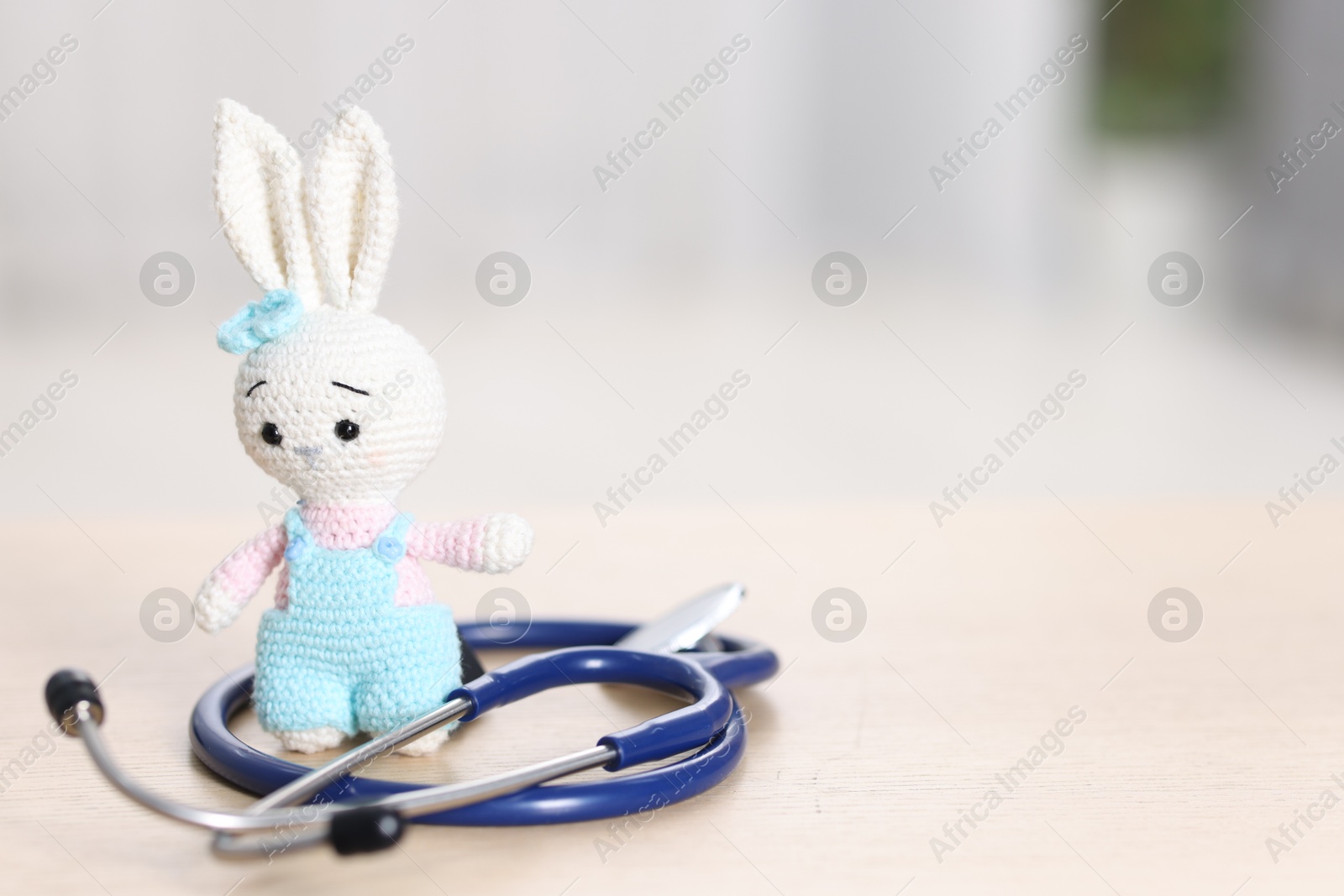 Photo of Pediatrics concept. Toy bunny with stethoscope on table indoors, space for text