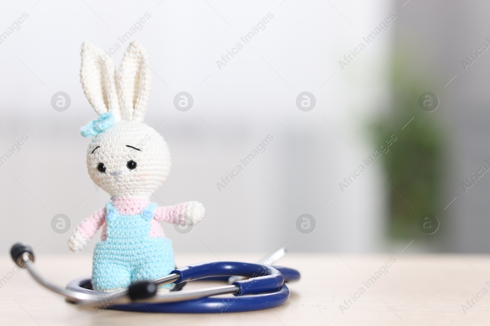 Photo of Pediatrics concept. Toy bunny with stethoscope on table indoors, space for text