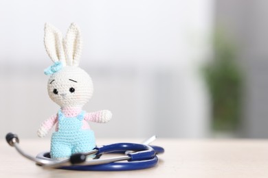 Photo of Pediatrics concept. Toy bunny with stethoscope on table indoors, space for text