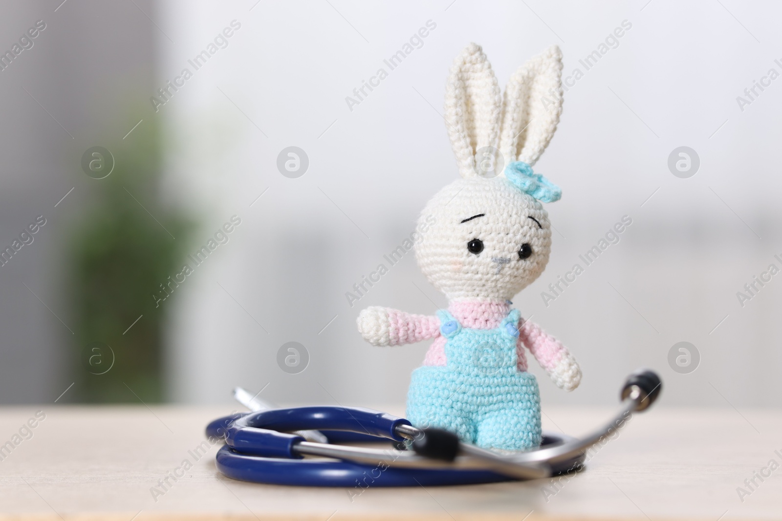 Photo of Pediatrics concept. Toy bunny with stethoscope on table indoors, space for text