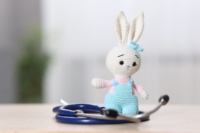 Photo of Pediatrics concept. Toy bunny with stethoscope on table indoors, space for text