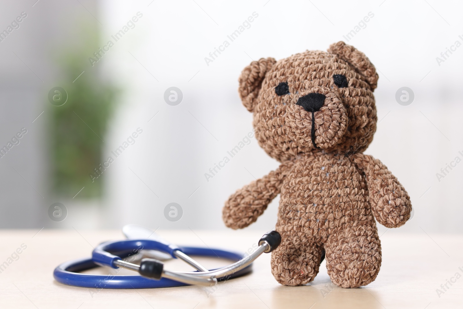 Photo of Pediatrics concept. Toy bear with stethoscope on table indoors, space for text