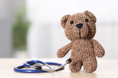 Photo of Pediatrics concept. Toy bear with stethoscope on table indoors, space for text