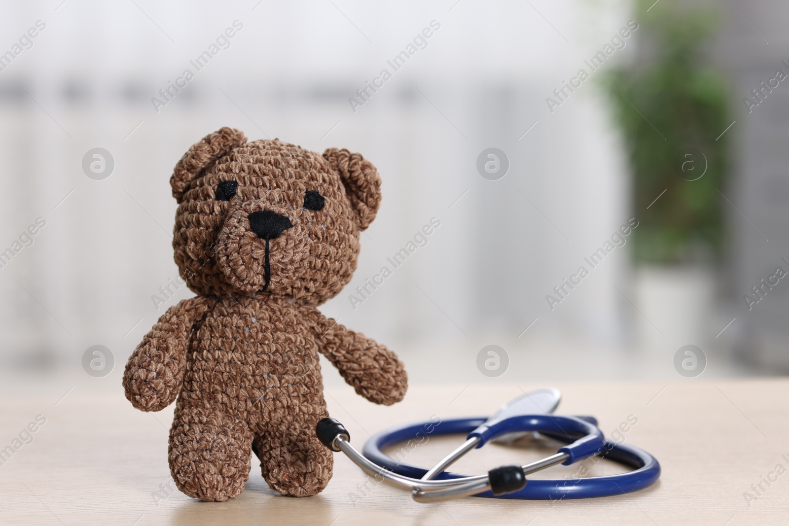 Photo of Pediatrics concept. Toy bear with stethoscope on table indoors, space for text