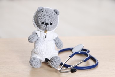 Photo of Pediatrics concept. Toy bear with stethoscope on wooden table indoors