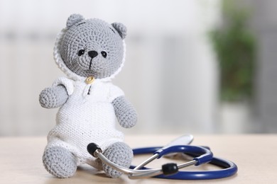 Photo of Pediatrics concept. Toy bear with stethoscope on table indoors, space for text