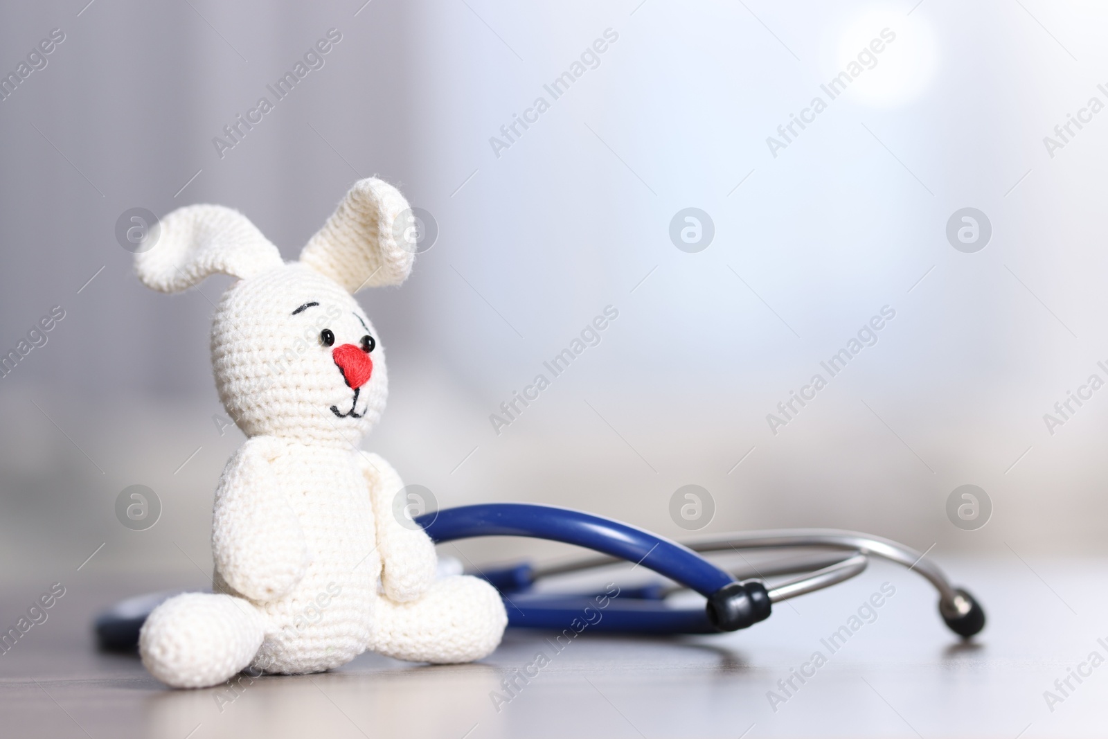 Photo of Pediatrics concept. Toy bunny with stethoscope on table indoors, space for text