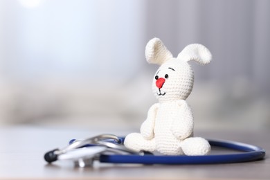 Photo of Pediatrics concept. Toy bunny with stethoscope on table indoors, space for text