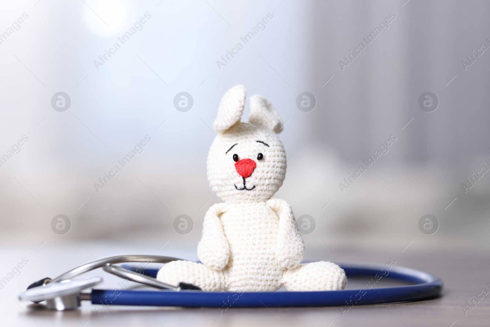 Photo of Pediatrics concept. Toy bunny with stethoscope on table indoors