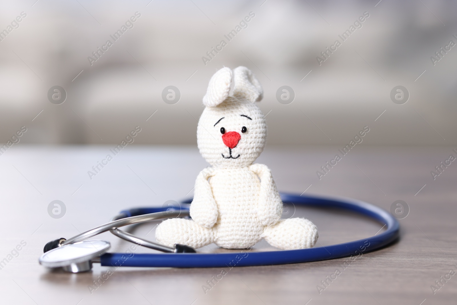 Photo of Pediatrics concept. Toy bunny with stethoscope on table indoors