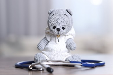 Photo of Pediatrics concept. Toy bear with stethoscope on table indoors