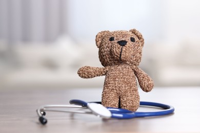 Photo of Pediatrics concept. Toy bear with stethoscope on table indoors, space for text