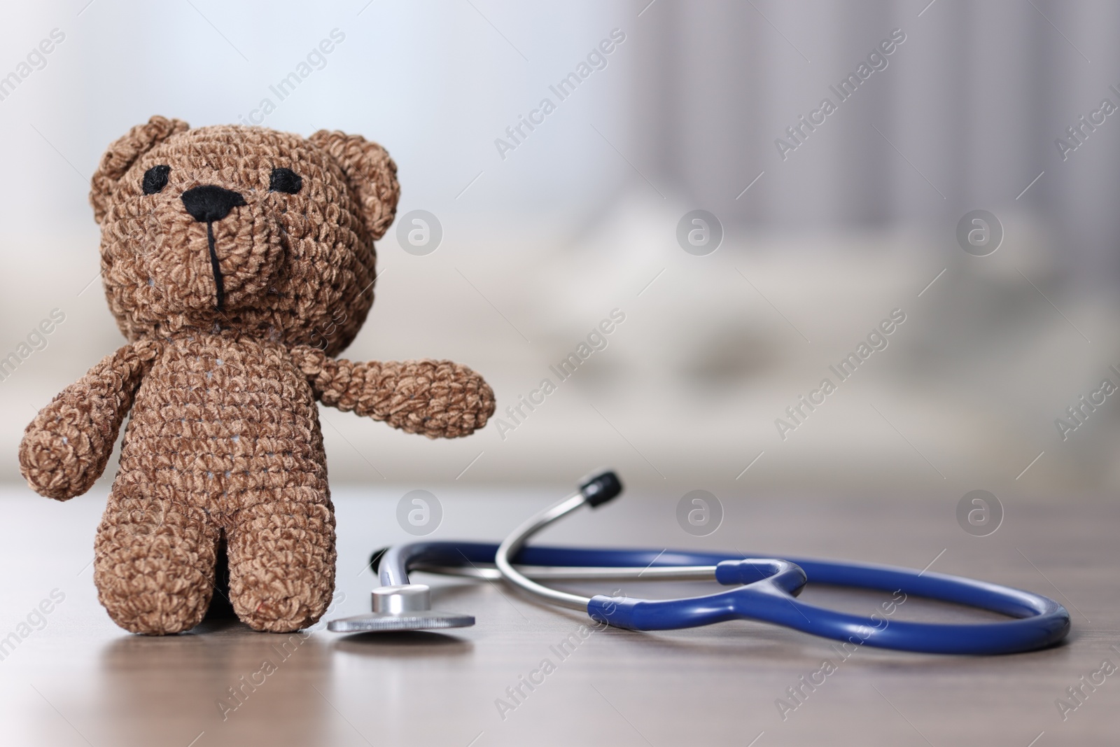 Photo of Pediatrics concept. Toy bear with stethoscope on table indoors, space for text