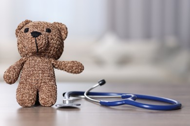 Photo of Pediatrics concept. Toy bear with stethoscope on table indoors, space for text