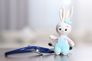 Photo of Pediatrics concept. Toy bunny with stethoscope on table indoors, space for text