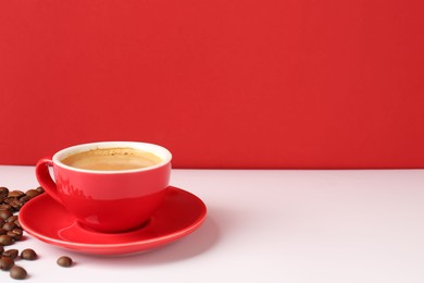 Red cup with coffee and roasted beans on white table, space for text