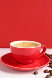 Red cup with coffee and roasted beans on white table, space for text