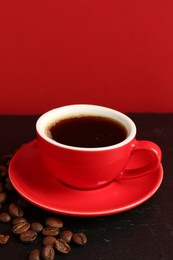 Photo of Red cup with coffee and roasted beans on black table