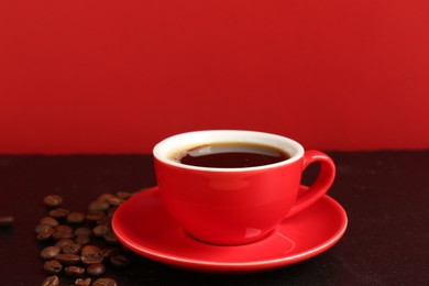 Photo of Red cup with coffee and roasted beans on black table