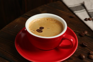 Photo of Red cup with coffee and roasted beans on wooden table, closeup