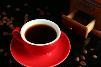 Photo of Red cup with coffee, vintage grinder and roasted beans on black background, closeup