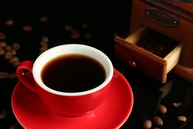 Photo of Red cup with coffee, vintage grinder and roasted beans on black background, closeup