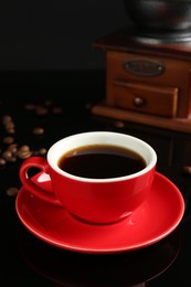 Photo of Red cup with coffee, vintage grinder and roasted beans on black background