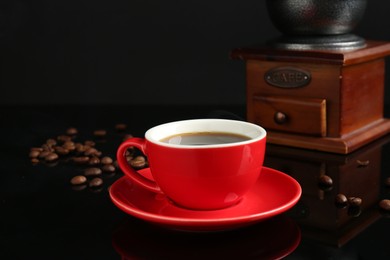 Photo of Red cup with coffee, vintage grinder and roasted beans on black background