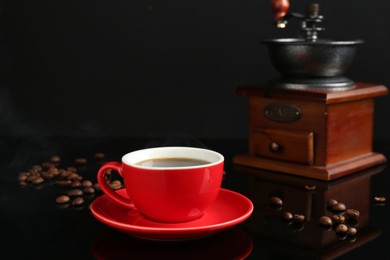 Photo of Red cup with coffee, vintage grinder and roasted beans on black background