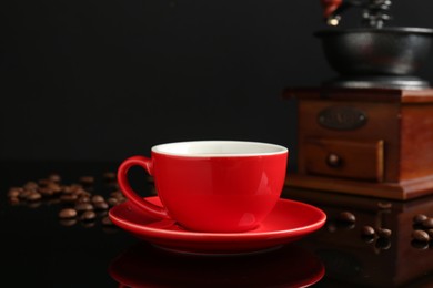 Photo of Red cup with coffee, vintage grinder and roasted beans on black background