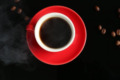 Photo of Red cup with coffee and roasted beans on black background, top view