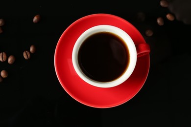 Photo of Red cup with coffee and roasted beans on black background, top view