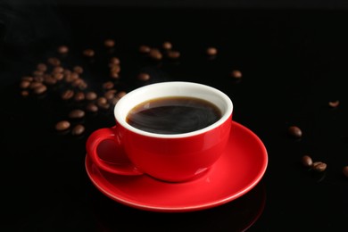 Photo of Red cup with coffee and roasted beans on black background