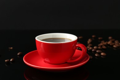 Photo of Red cup with coffee and roasted beans on black background