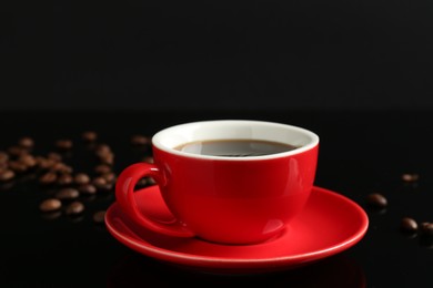 Photo of Red cup with coffee and roasted beans on black background, closeup