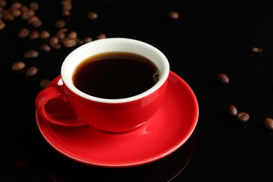 Photo of Red cup with coffee and roasted beans on black background, closeup