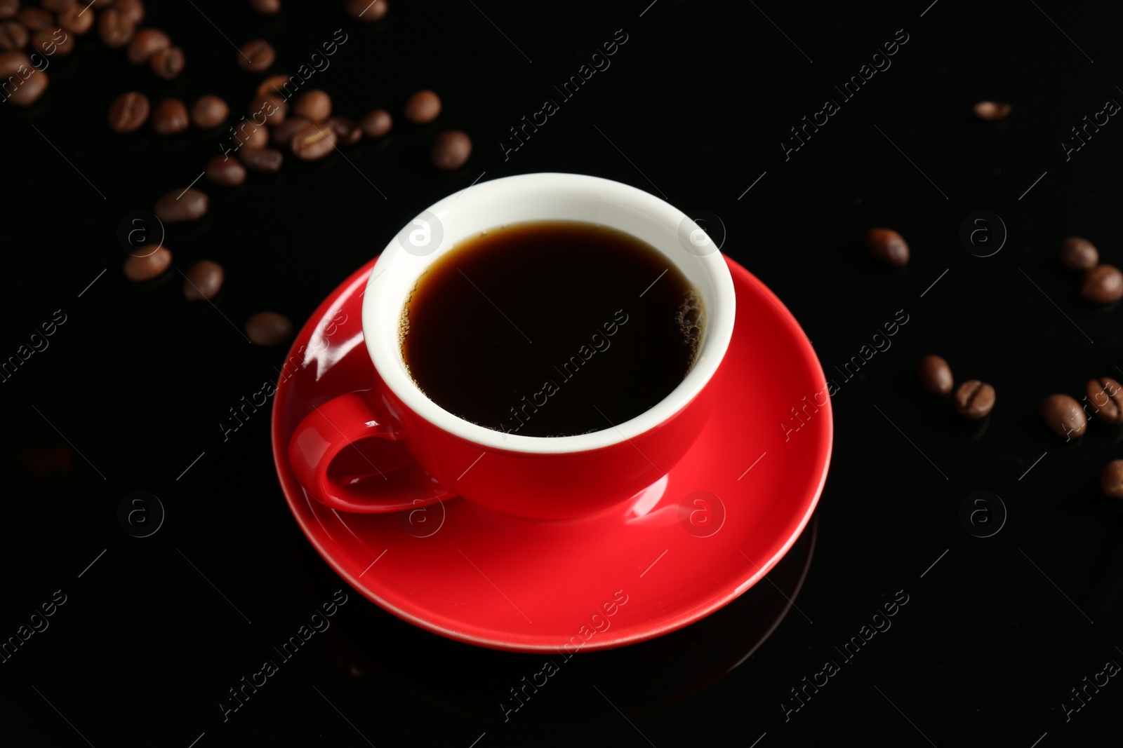 Photo of Red cup with coffee and roasted beans on black background