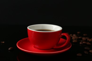 Photo of Red cup with coffee and roasted beans on black background, closeup