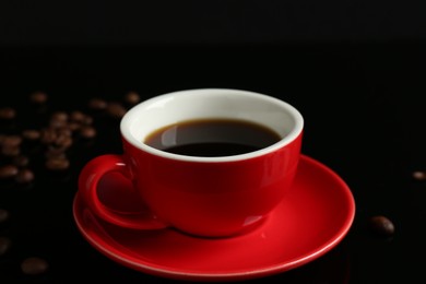 Photo of Red cup with coffee and roasted beans on black background, closeup