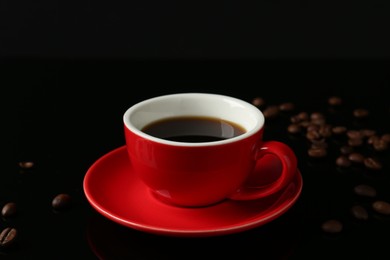 Photo of Red cup with coffee and roasted beans on black background, closeup