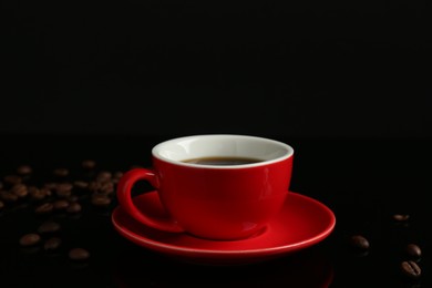 Photo of Red cup with coffee and roasted beans on black background